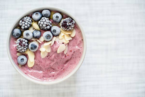 A bowl filled with pink smoothie, topped with frozen berries and nuts
