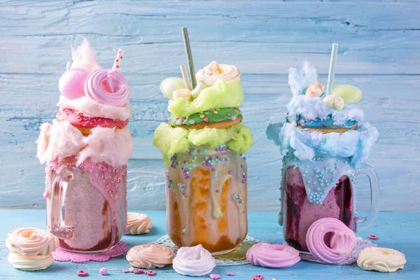 Three pastel colored milkshakes, all topped with a donut, candy floss, meringue and more candy