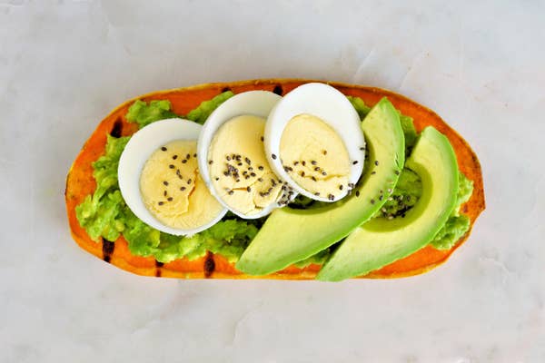 A thin, long piece of sweet potato that's been toasted and covered with egg and avocado