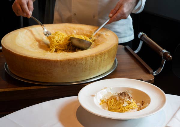 A wheel of cheese is hollowed out, with spaghetti in the centre that someone is serving into a bowl
