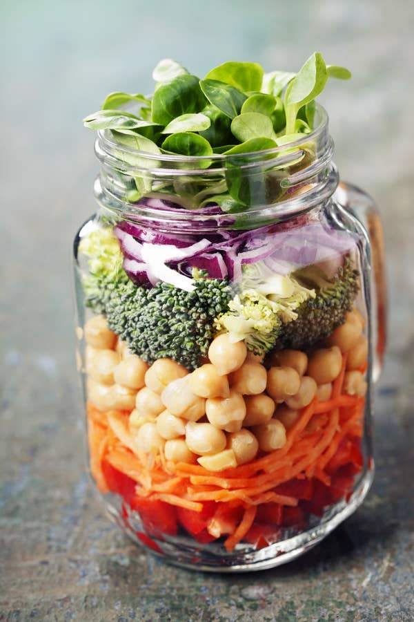 A clear jar filled with layers of vegetables and chickpeas,