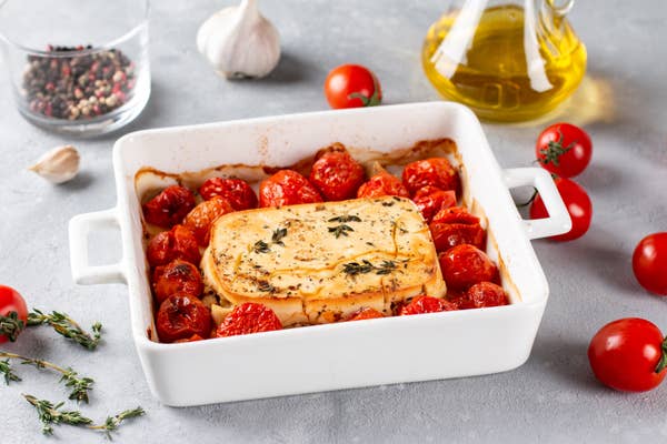 A baking dish with a block of feta at the centre, surrounded by baked cherry tomatoes