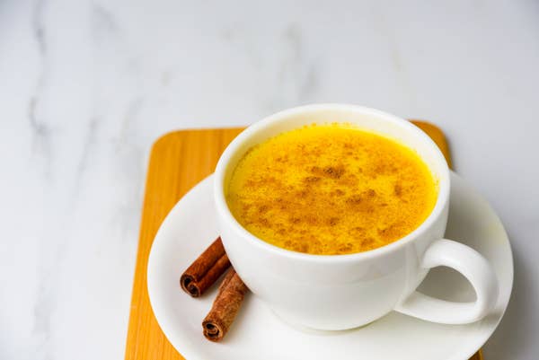 A bright yellow drink in a white mug, topped with cinnamon