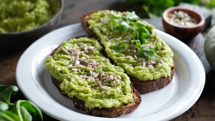 Two pieces of toast covered in mashed avocado and pumpkin seeds