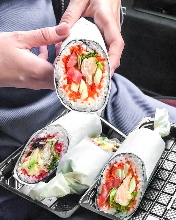 Someone holding a roll with rice on the outside, filled with fish and vegetables