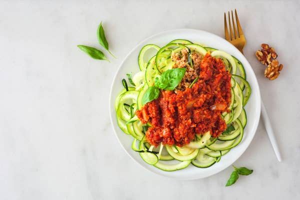 A bowl filled with thinly shredded zucchni, topped with a bolognese tomato sauce