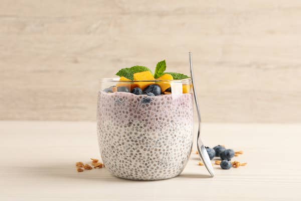 A glass filled with yoghurt and chia seeds, with fresh mango and blueberries on top
