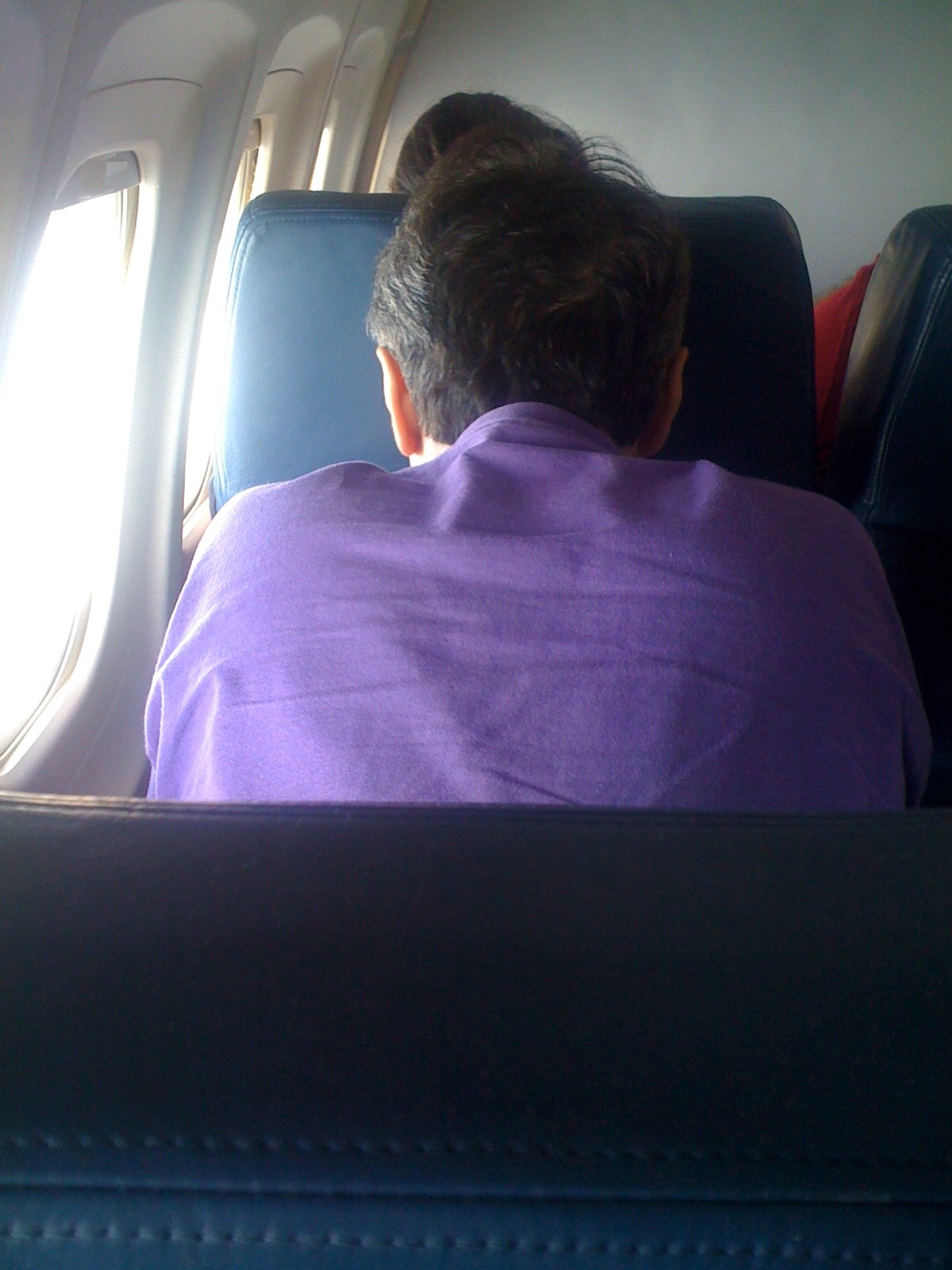 The back of someone leaning forward in their airplane seat