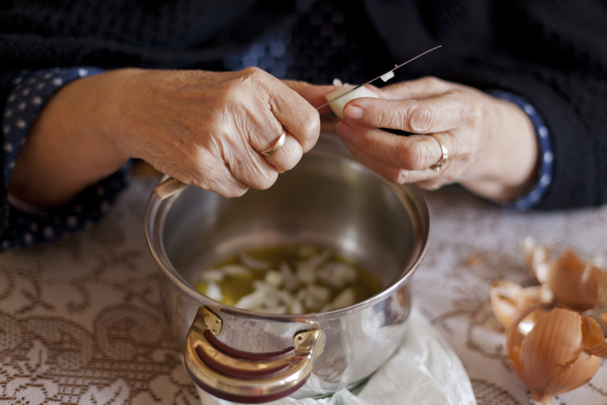 An older woman cutting food and dropping it into a pot.