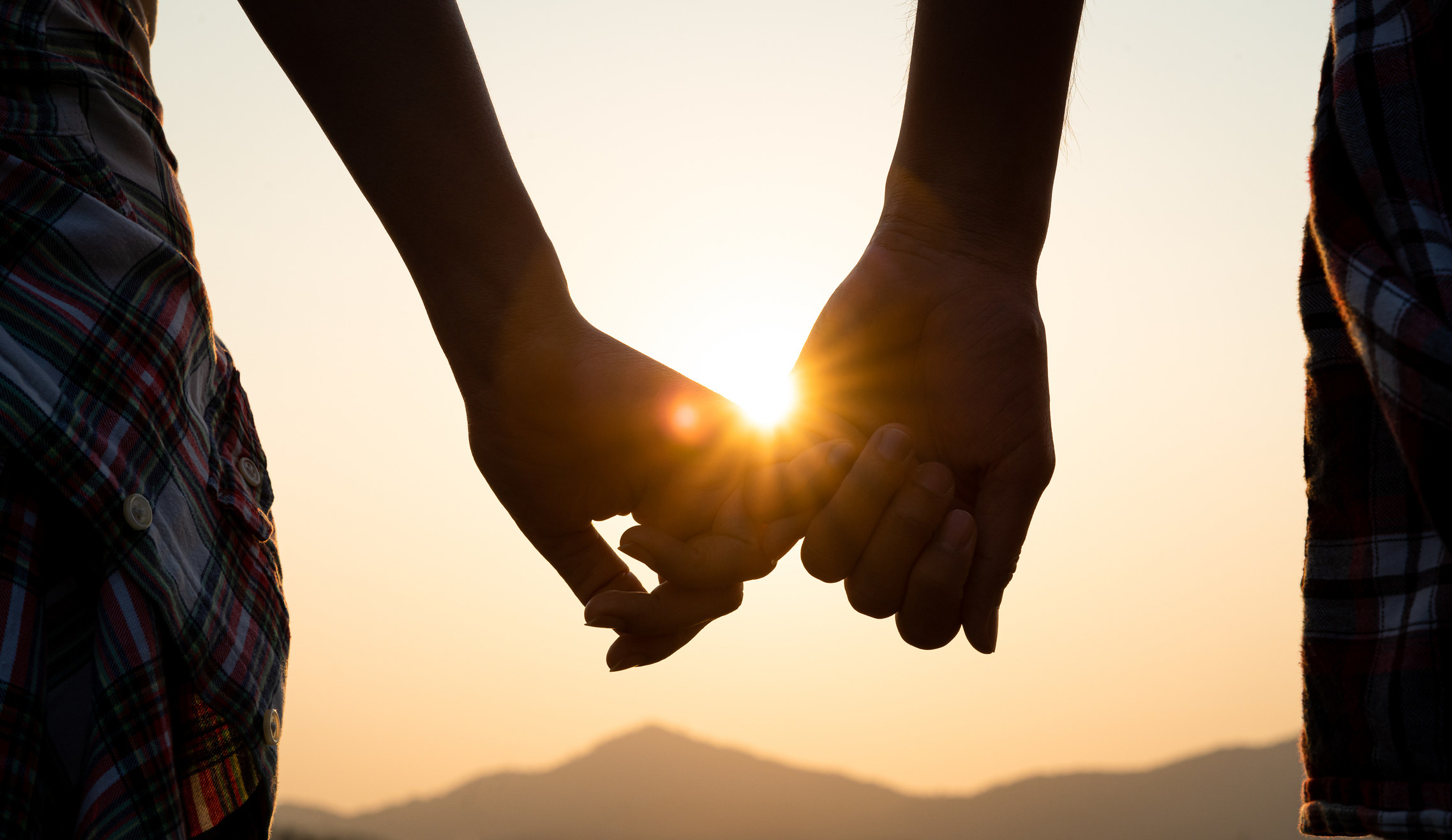 A couple holding hands in front of the sun.