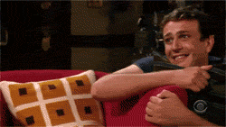 a gif of marshall from how I met your mother smiling and hiding bashfully behind a pillow