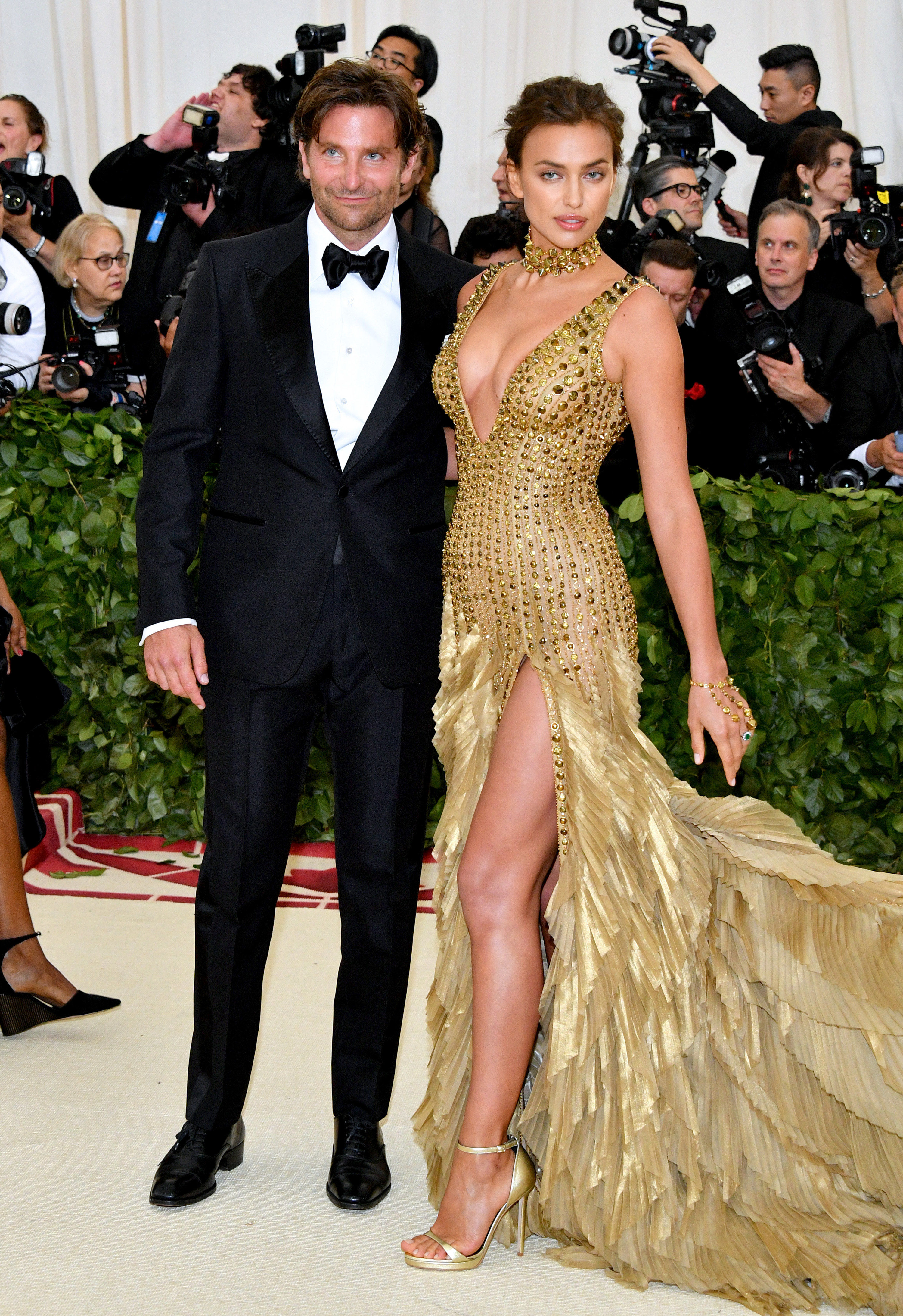 Bradley in a tux and Irina in an all-gold dress with sequins and a long train stand together