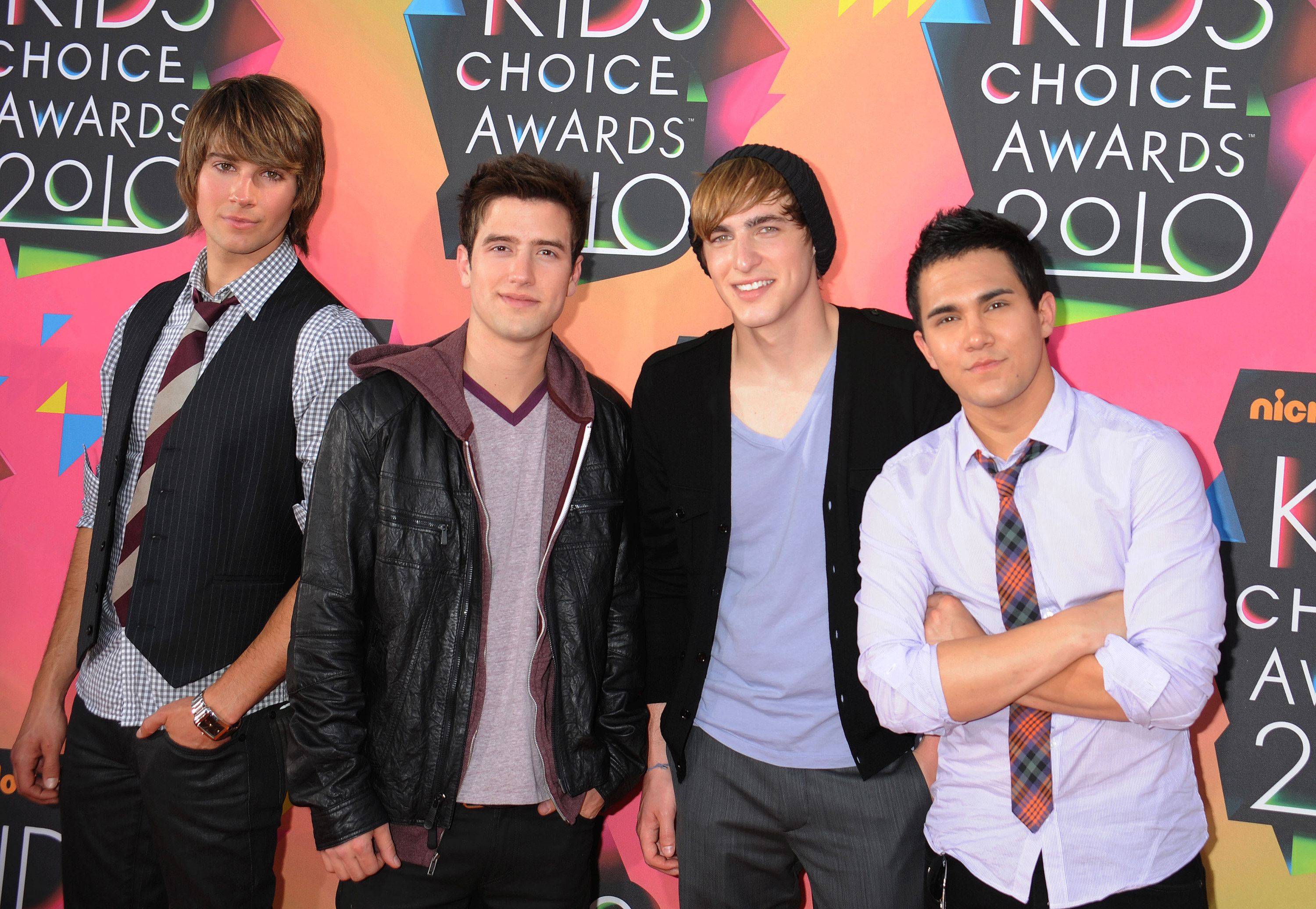 Four band members dressed casually in various vests, jackets, shirts, and ties
