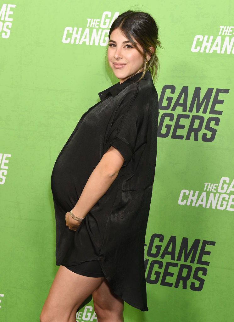 Daniella in a short dress and long shirt and showing a baby bump
