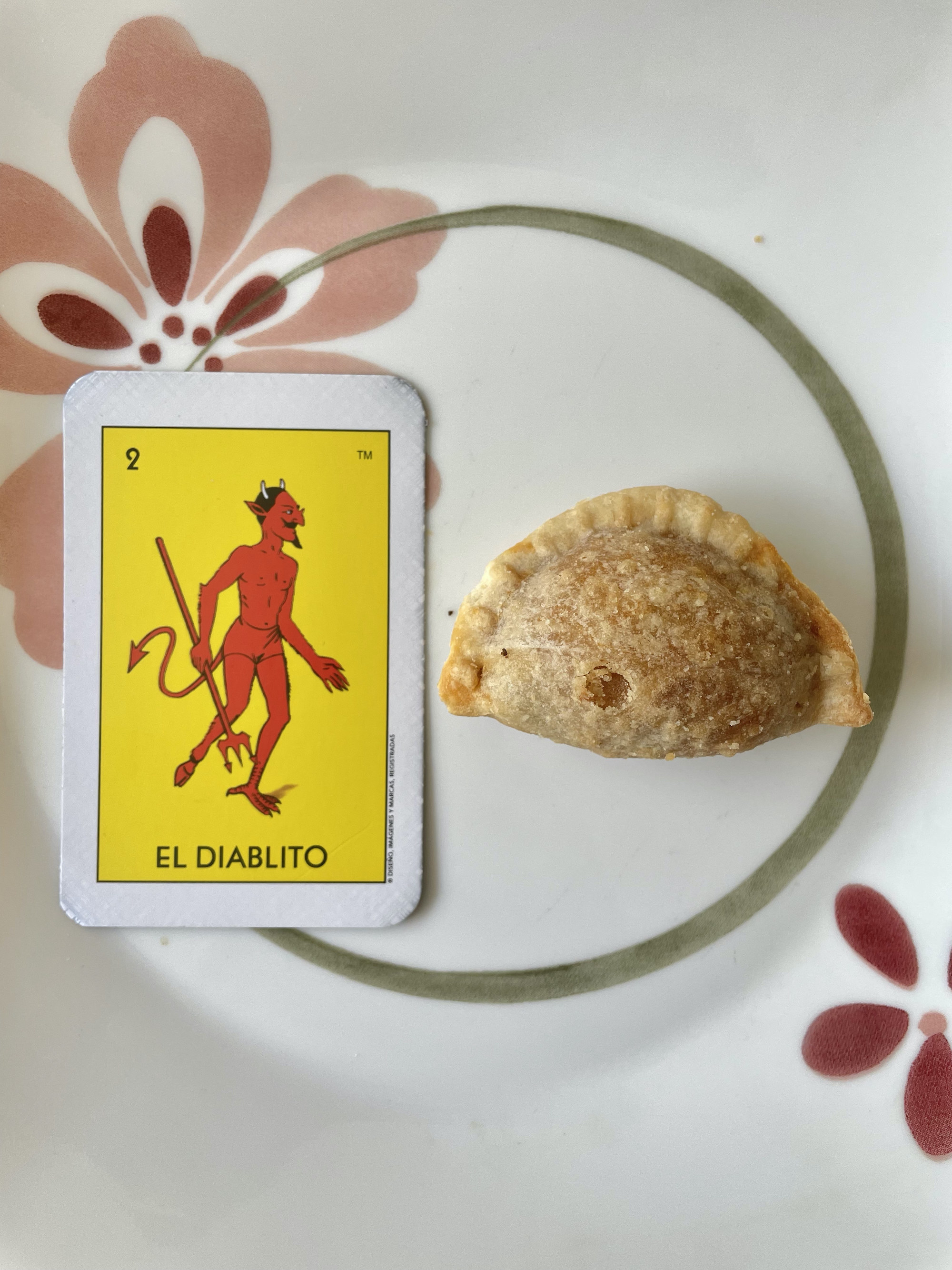 A Loteria card and the empanada on a plate, with the empanada being about half the length and the same width