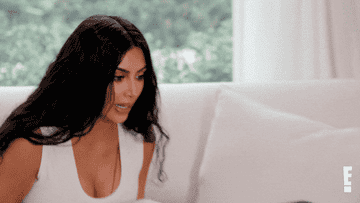 Kim Kardashian covers her mouth with her hand and sits back on a couch