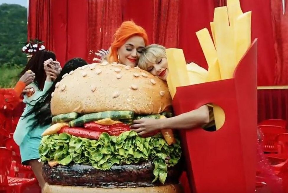 Katy Perry dressed as a hamburger hugs Taylor Swift, dressed as a box of fries