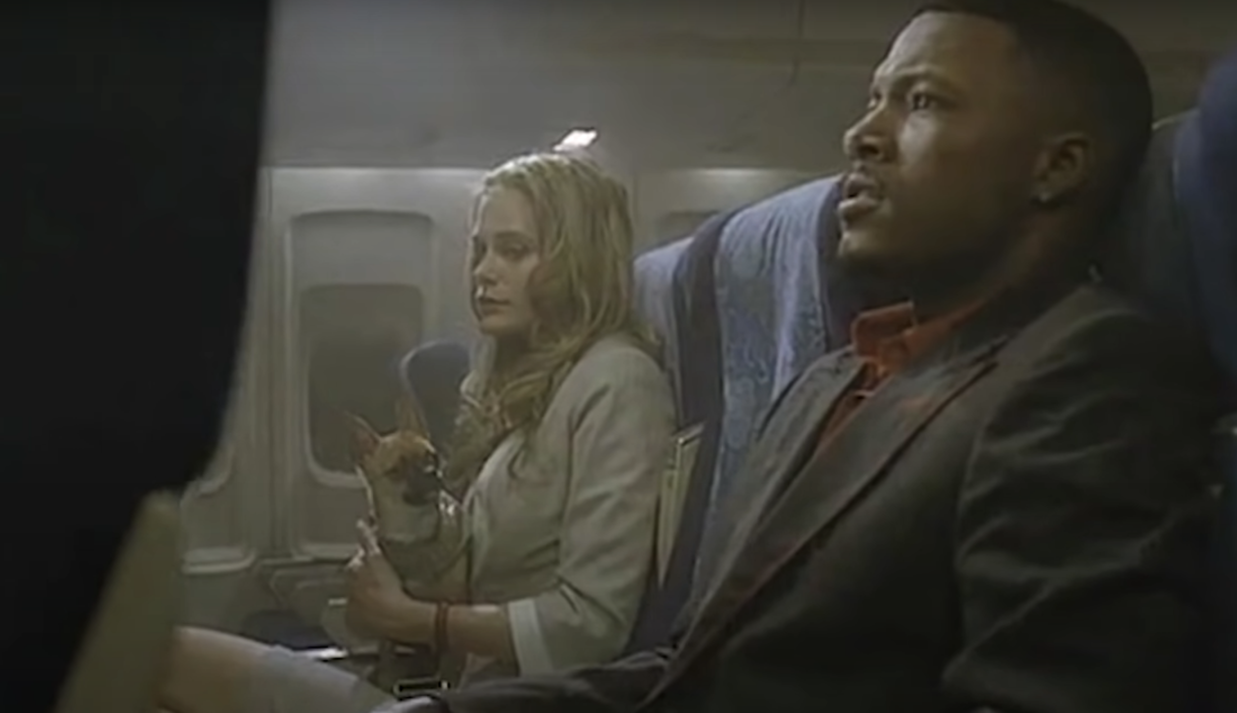 Two passengers and a tiny dog seated on a plane in &quot;Snakes on a Plane&quot;