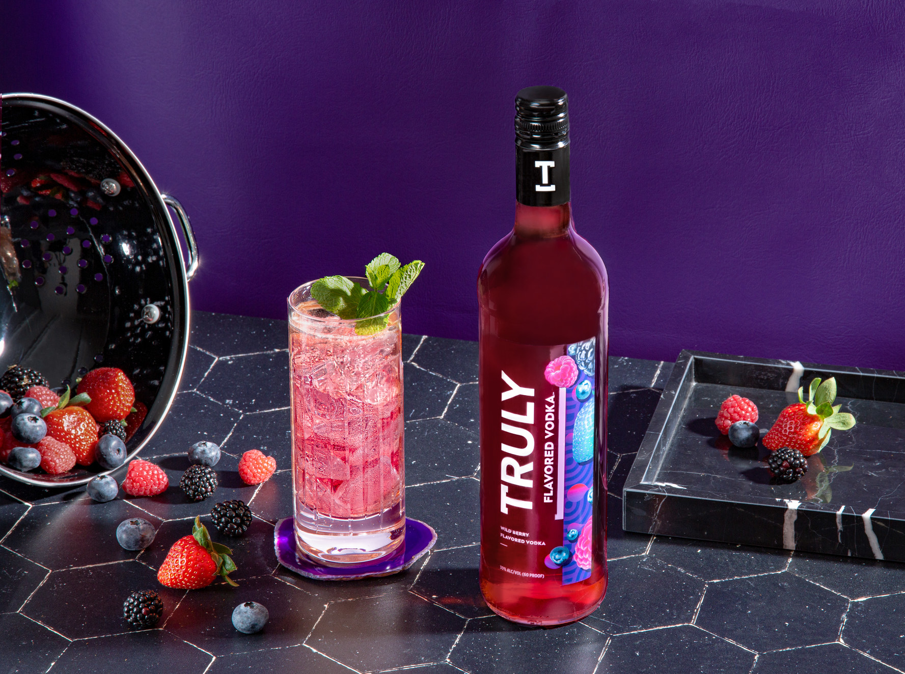 Truly Wild Berry Flavored Vodka next to cocktail and strawberries, blueberries, and blackberries