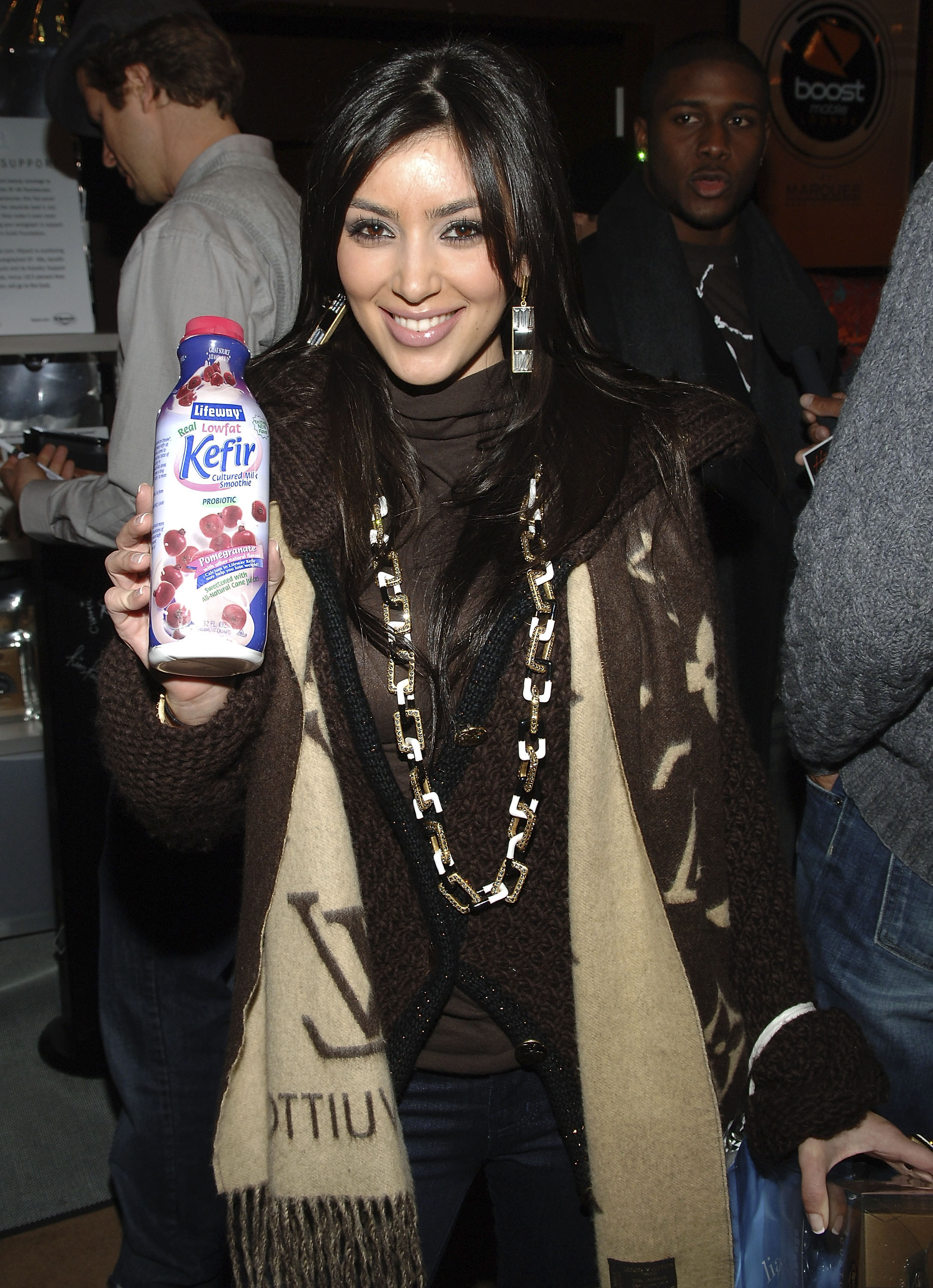 Kim wearing a long LV scarf while smiling and holding a bottle of Kefir