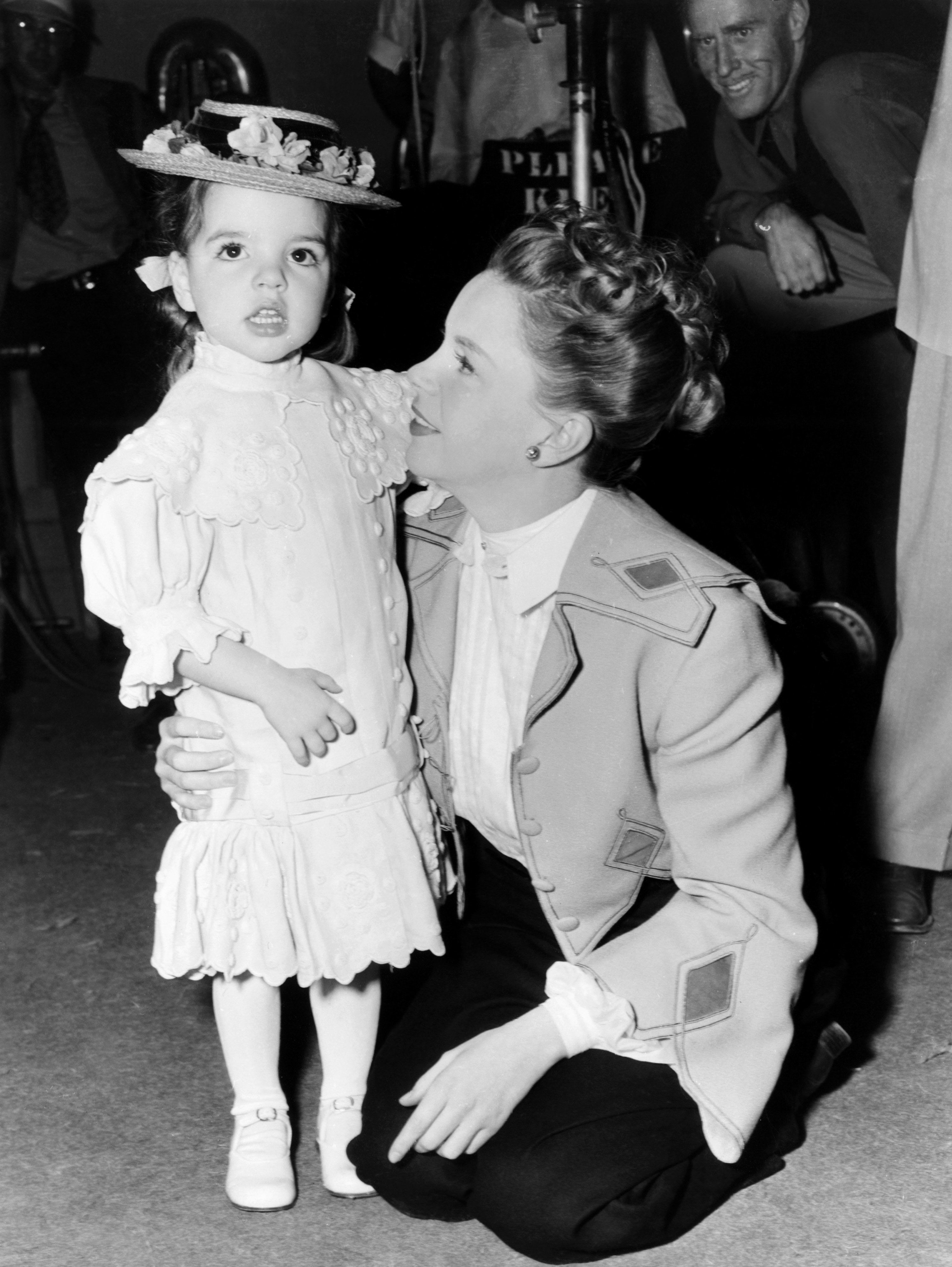 Judy leaning down with her arm around Liza wearing a dress and hat