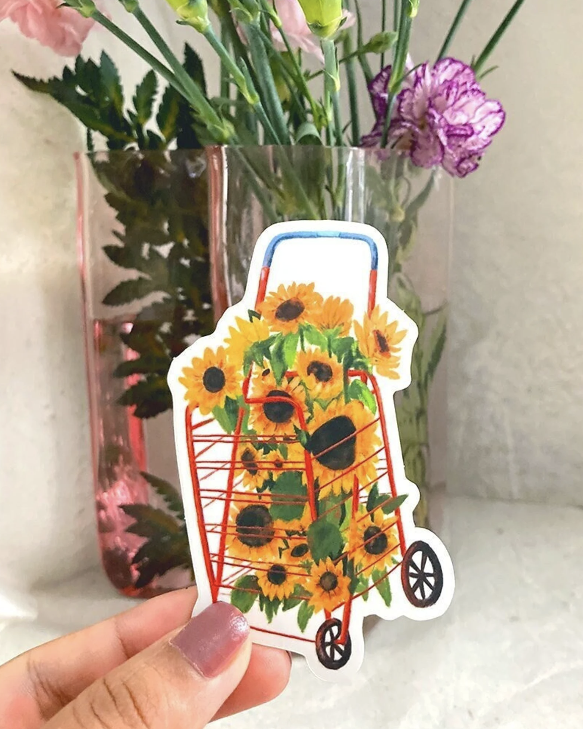 Hand holding a sticker of a cart filled with sunflowers.
