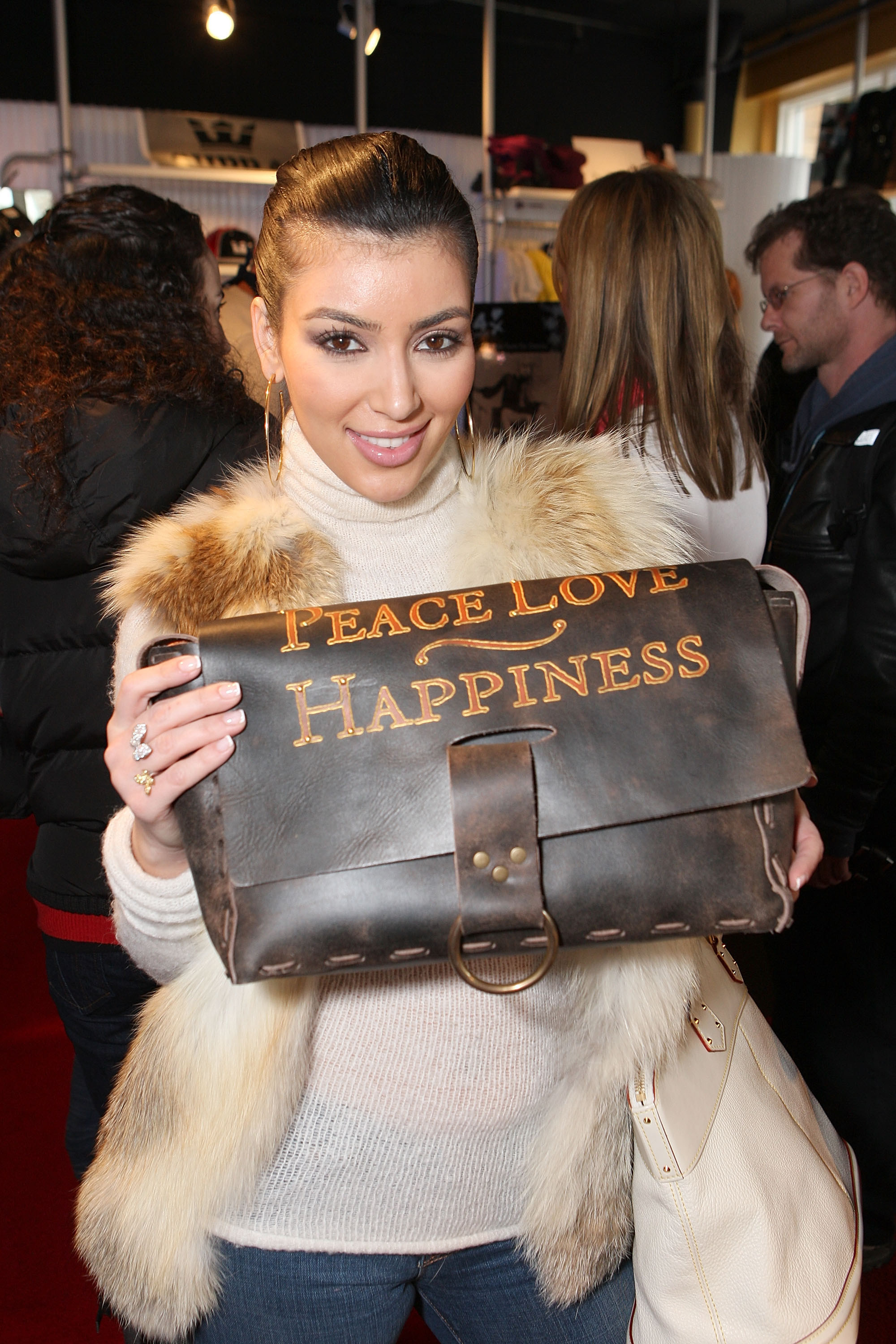 Kim holding a leather bag that says &quot;Peace, Love, Happiness&quot;