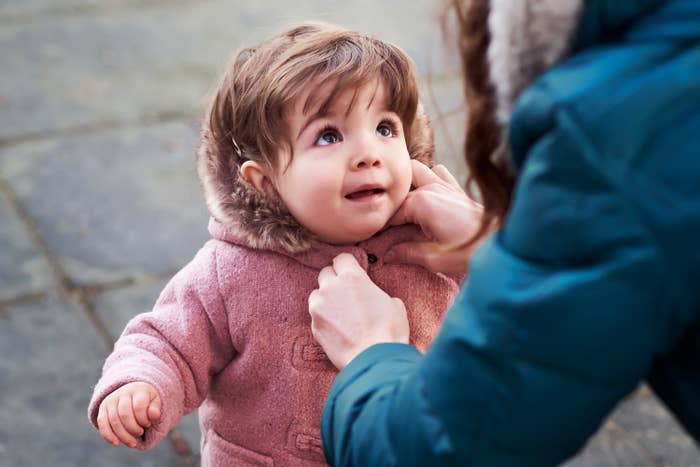 mom buttoning up a toddler&#x27;s coat