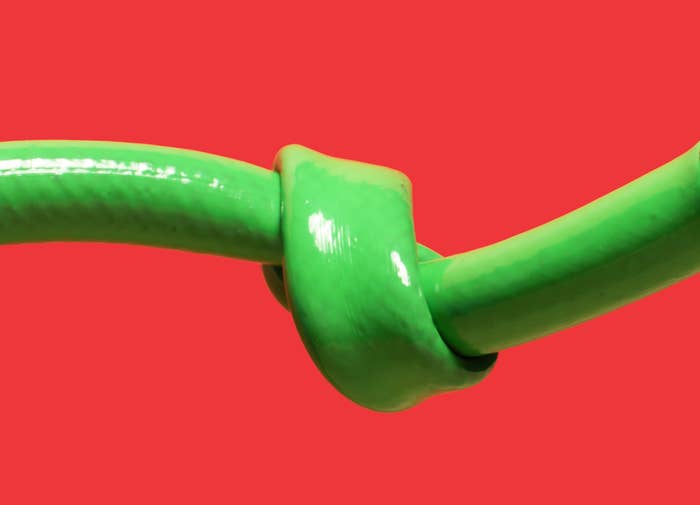 End of green garden hose with a knot in it, red background