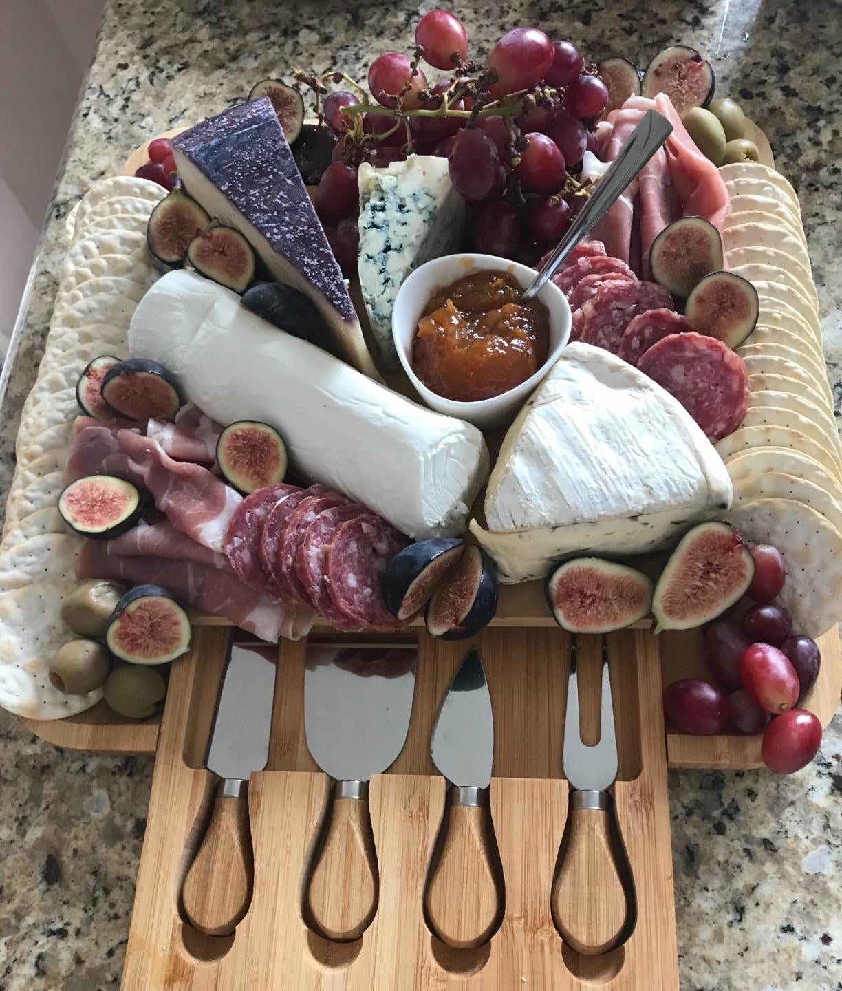 reviewer&#x27;s board artfully filled with cheeses, grapes, crackers and meat