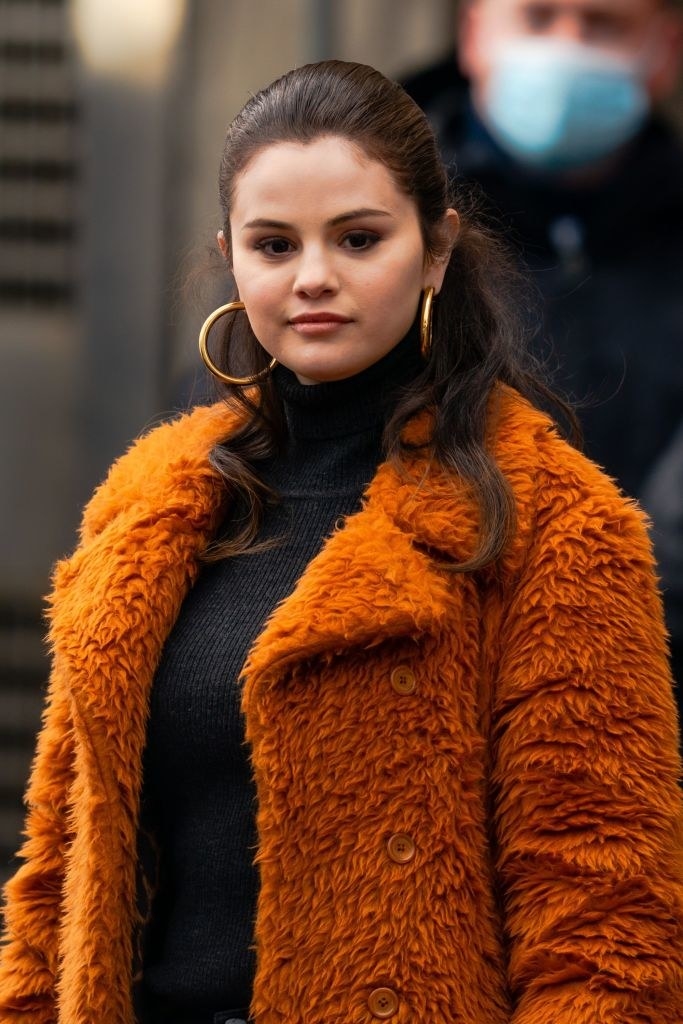 Selena wearing large hoop earrings and a furry coat