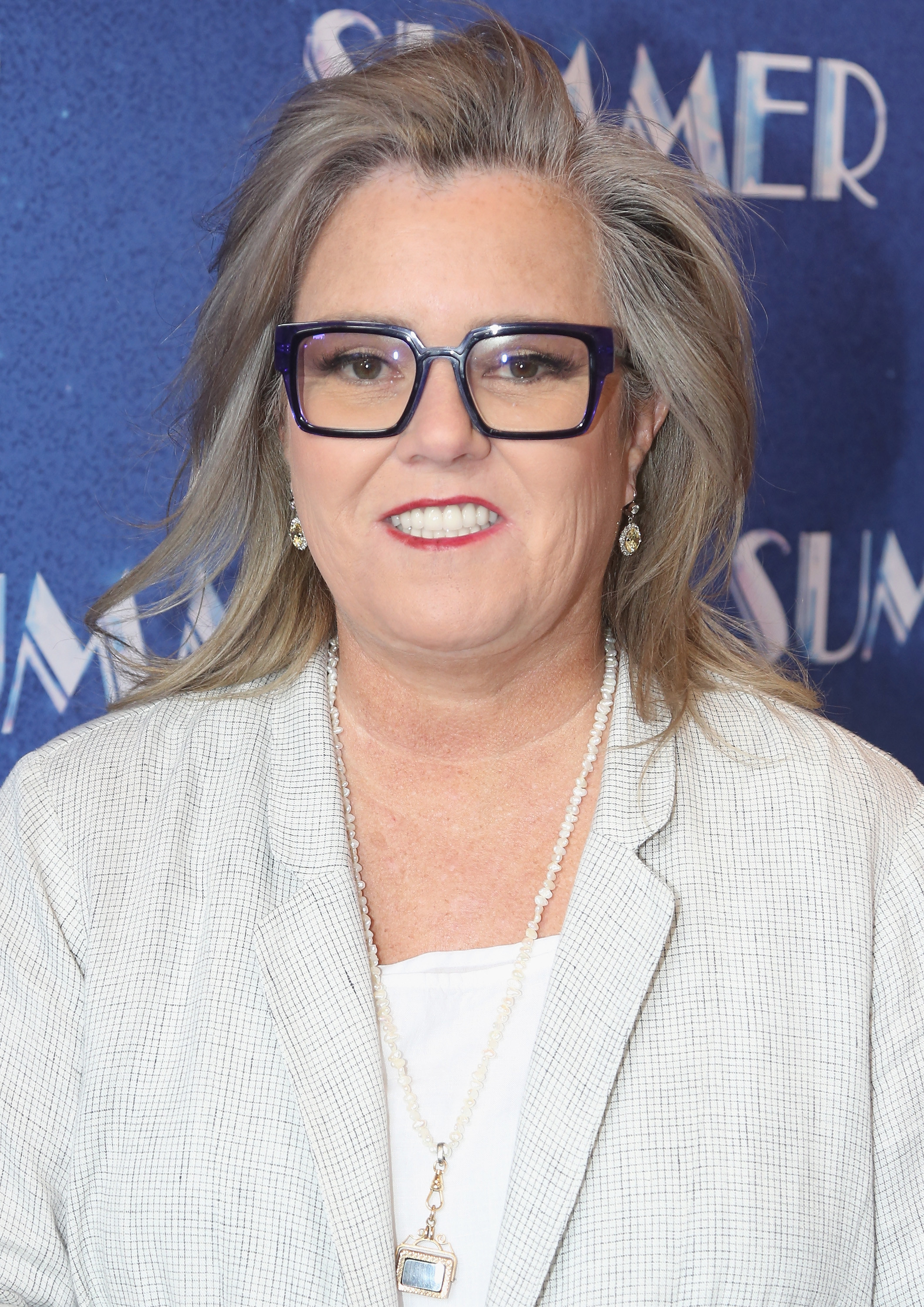 Rosie O&#x27;Donnell wears thick black glasses and a light grey suit jacket on a red carpet
