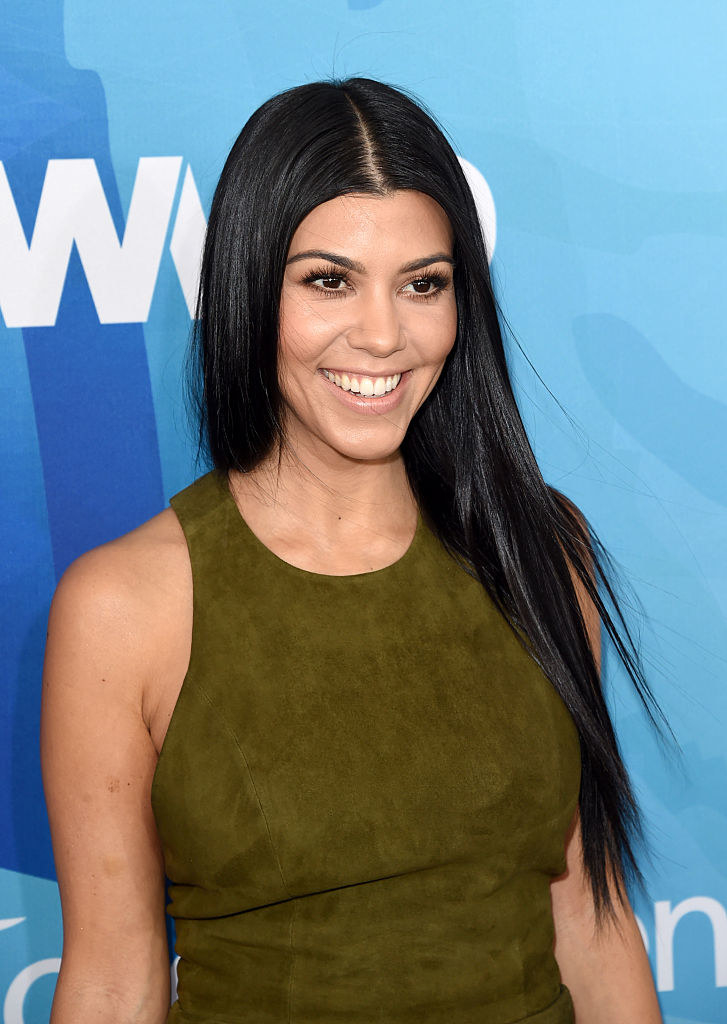 Smiling Kourtney in a sleeveless, suede-looking outfit