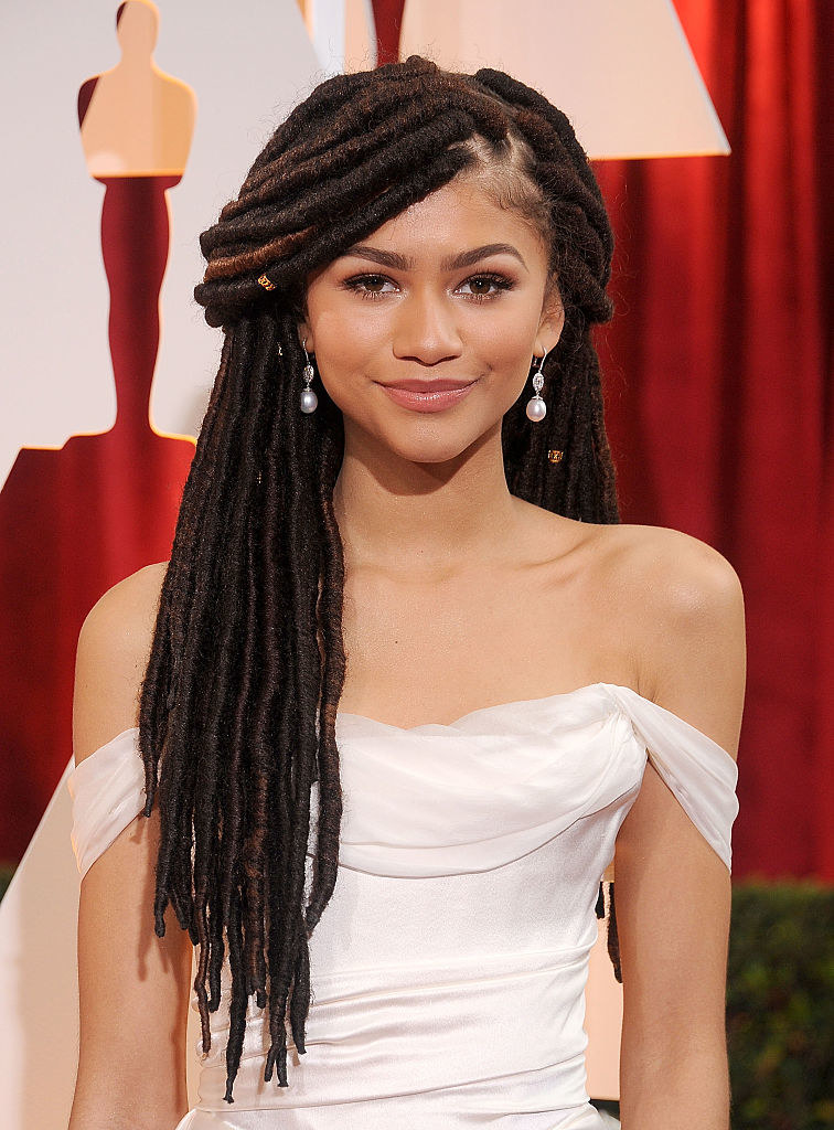 Smiling Zendaya wearing an off-the-shoulder gown and locs
