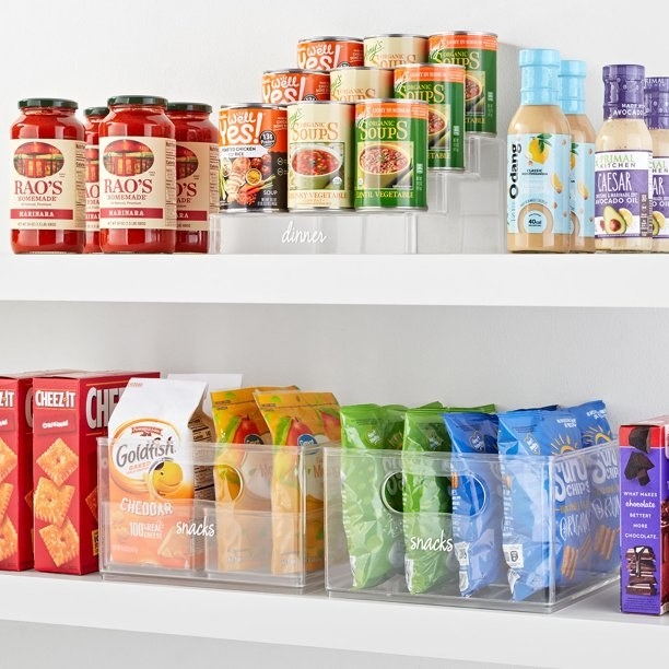 Clear bins and riser used in a pantry to hold various snacks and cans