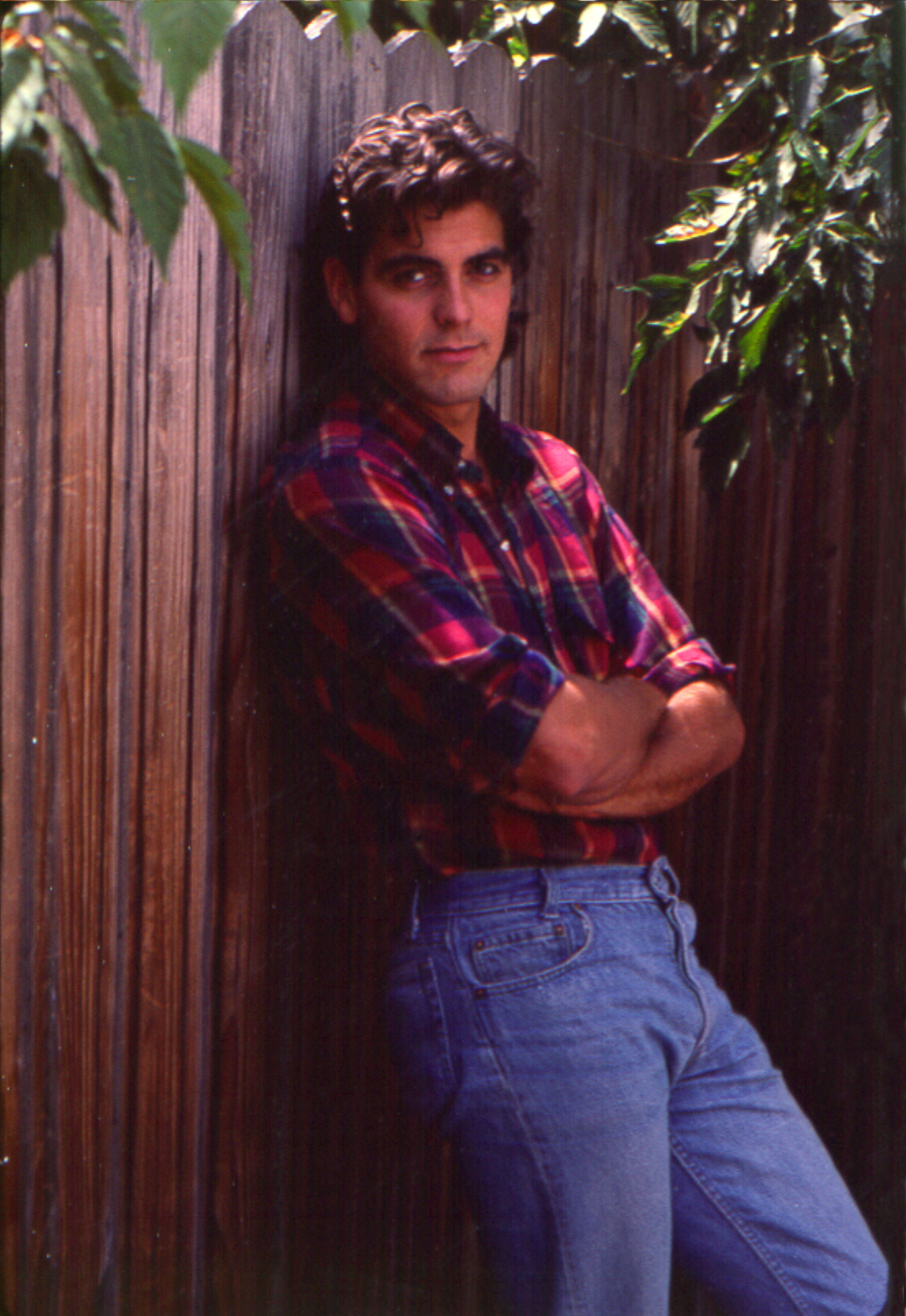 a young George leaning against a fence with jeans and a plaid shirt