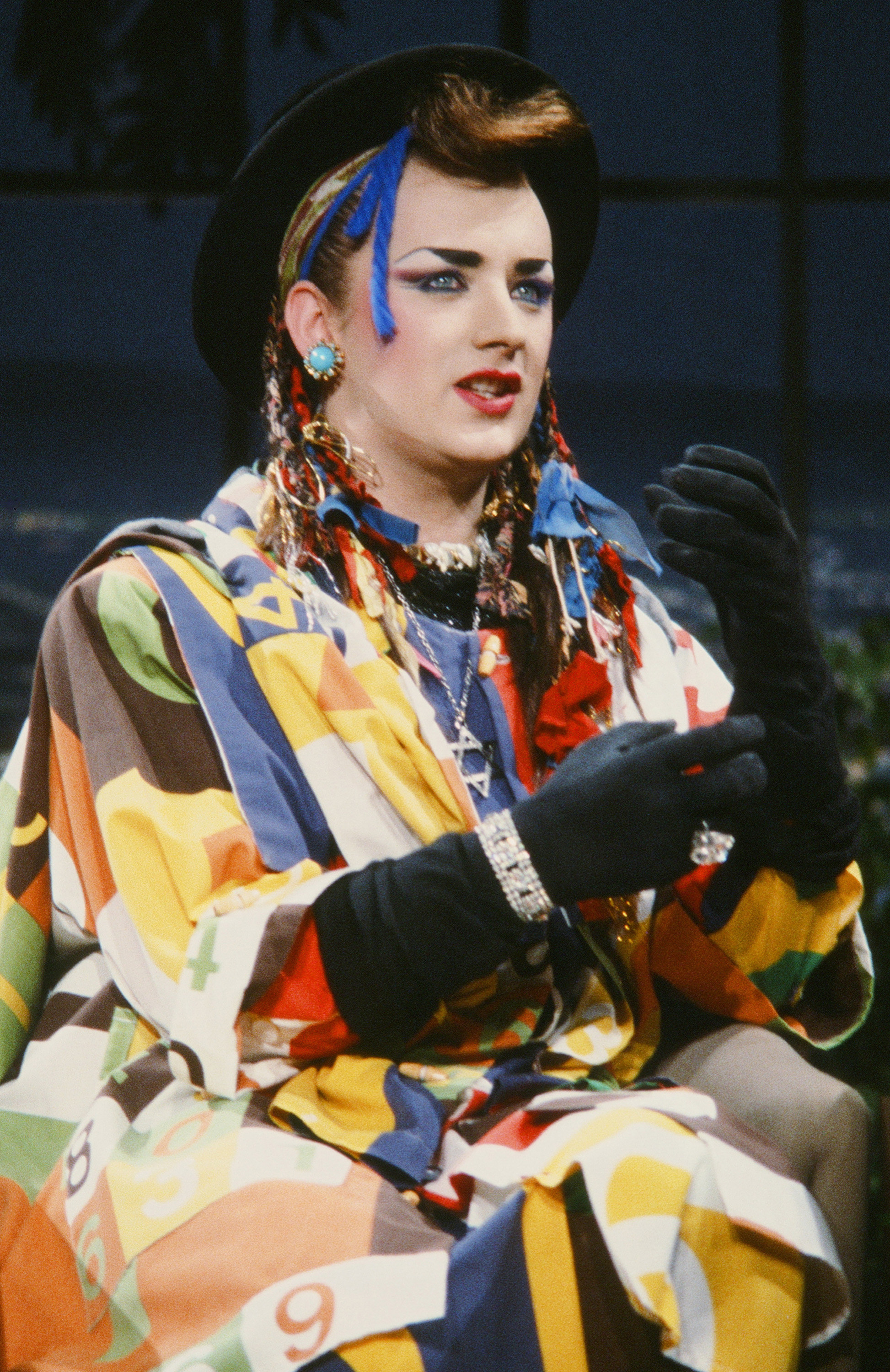 close up of Boy George in gloves, hair accessories and a hat