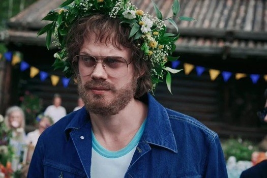 A bearded man wears glasses and a flower crown.