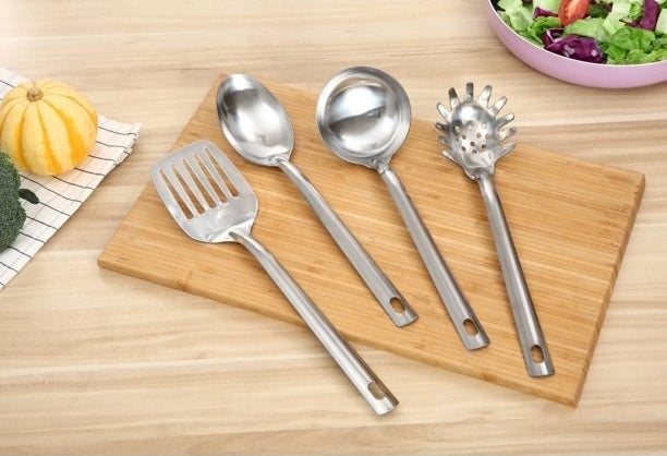 Four stainless steel kitchen utensils on a wood cutting board