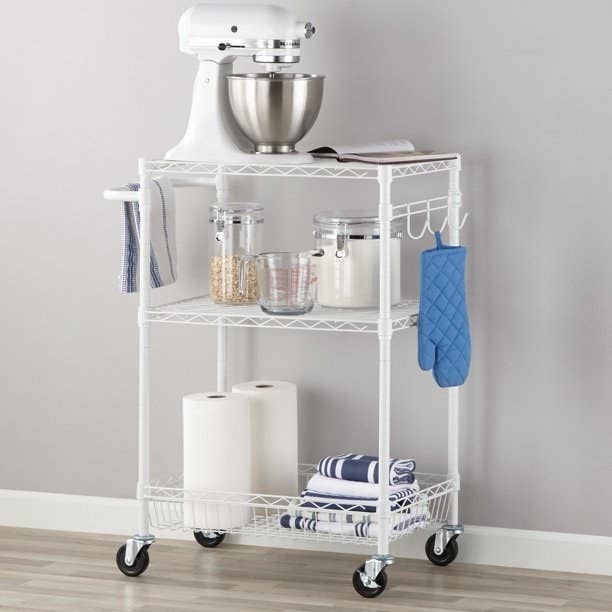 White cart with stand mixer on top and various canisters and kitchen items on shelves