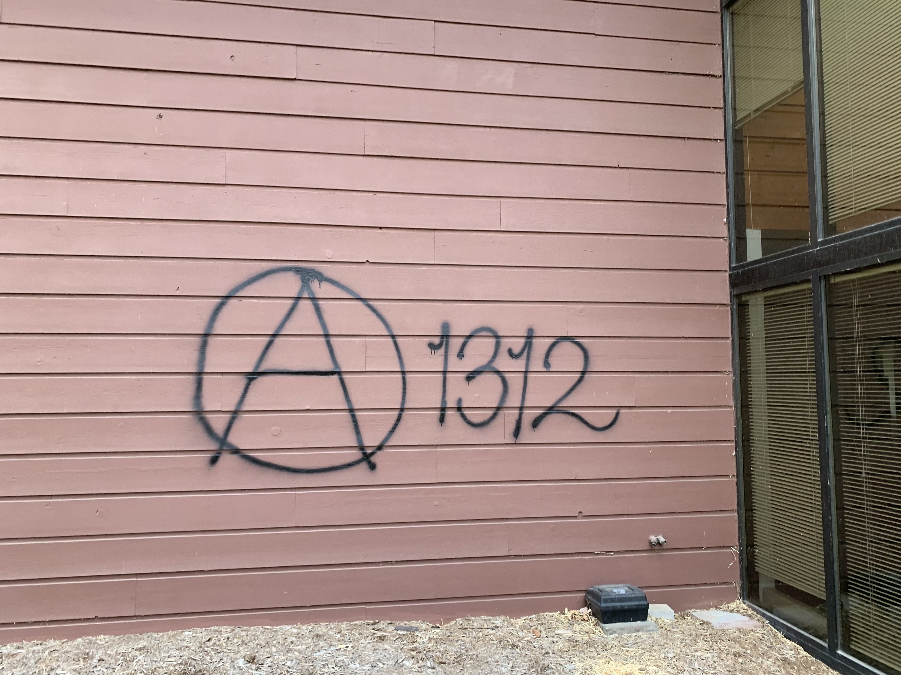 Graffiti on an exterior walls shows the letter A in a circle, with the numbers 1 3 1 2