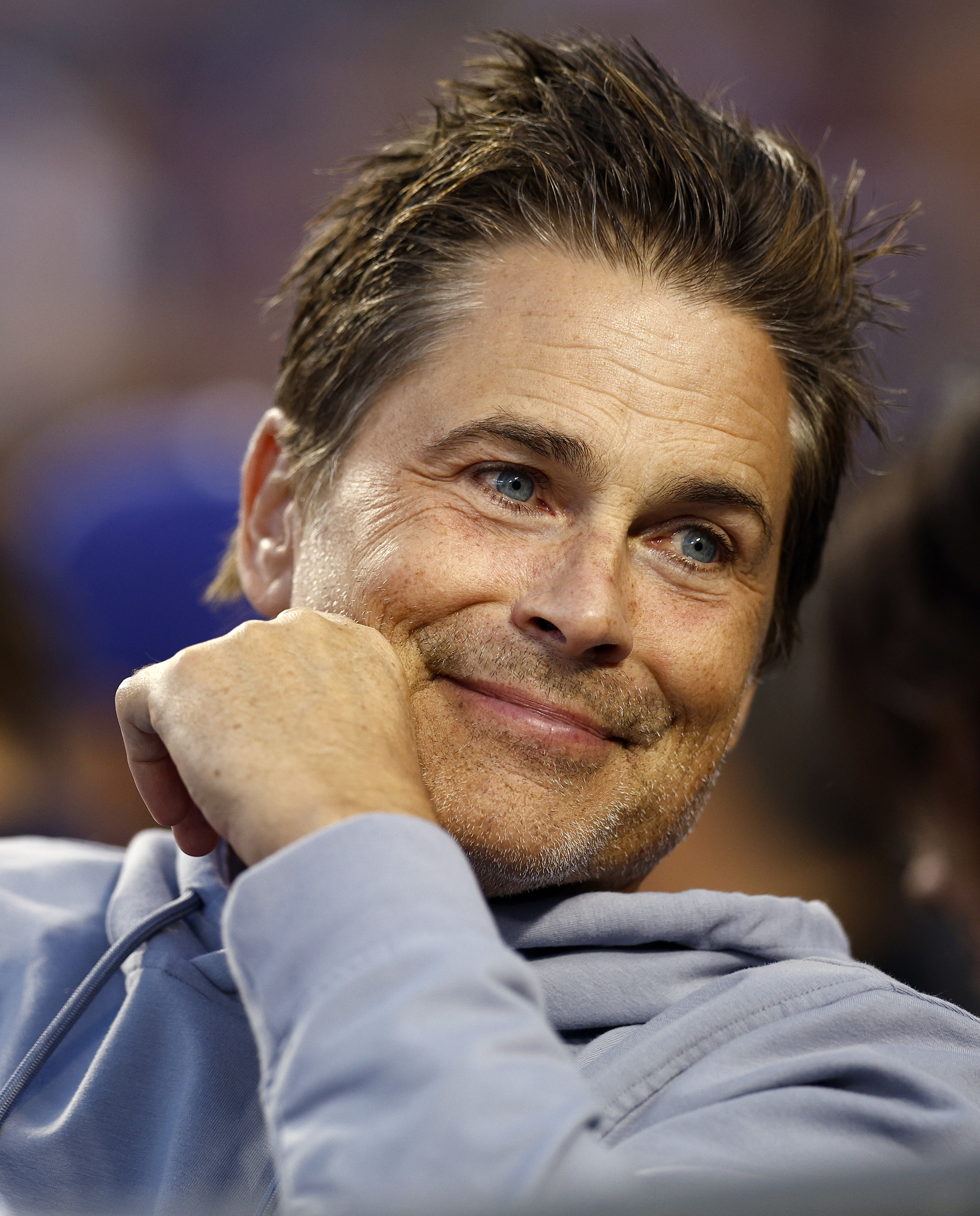 A closeup of Rob Lowe smiling while wearing a hoodie