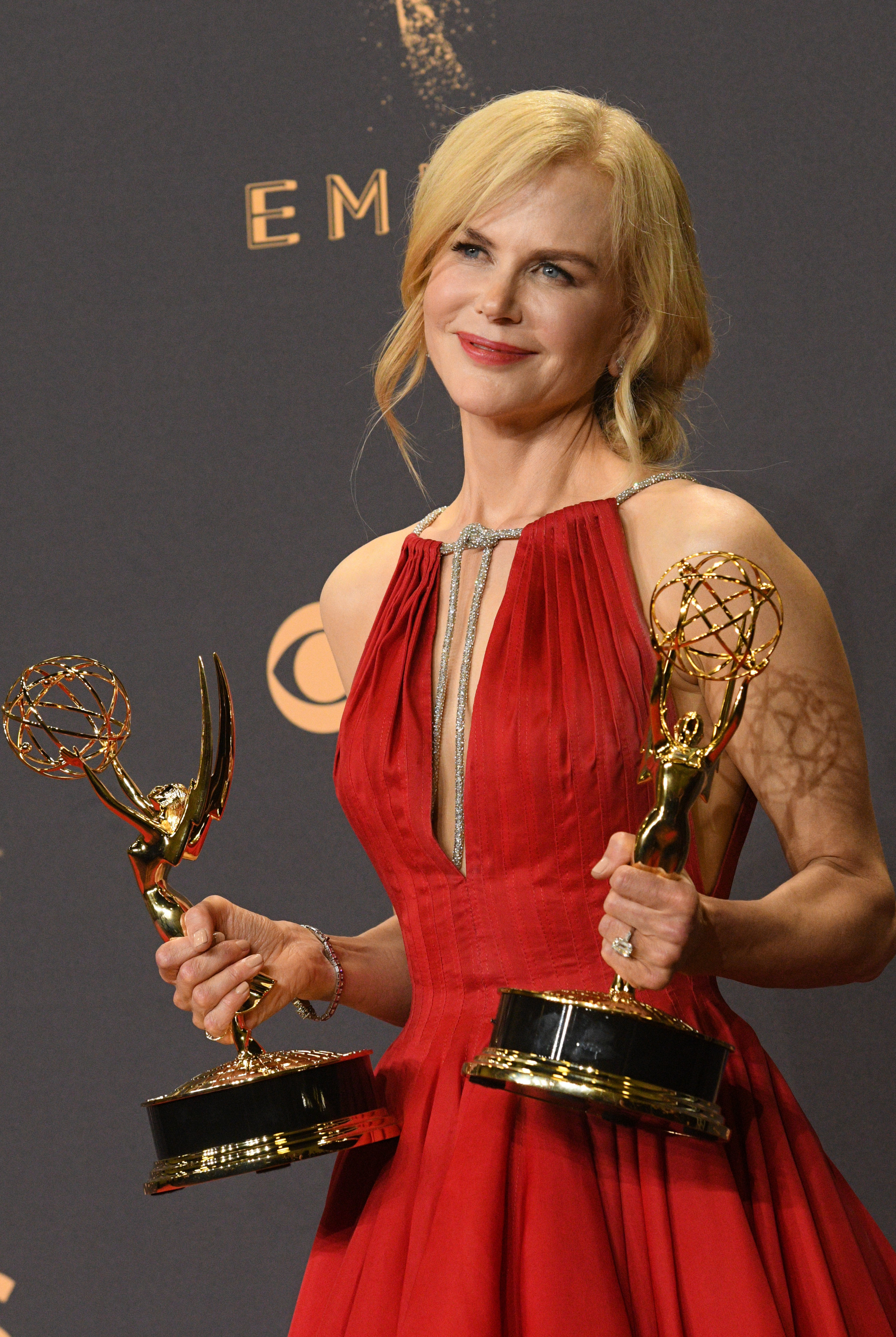 Nicole Kidman in a red dress holding two Emmys