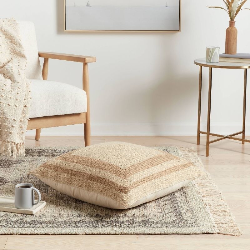 a square jute floor pillow on a rug next to an accent chair