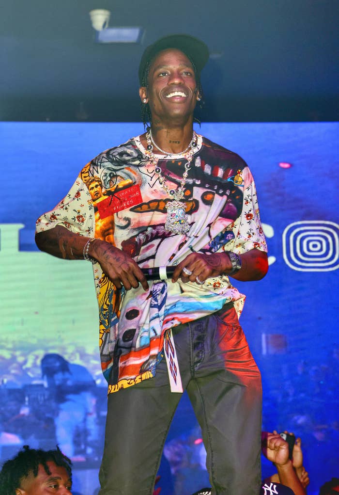 Travis Scott on stage holding a mic in front of a screen with his name