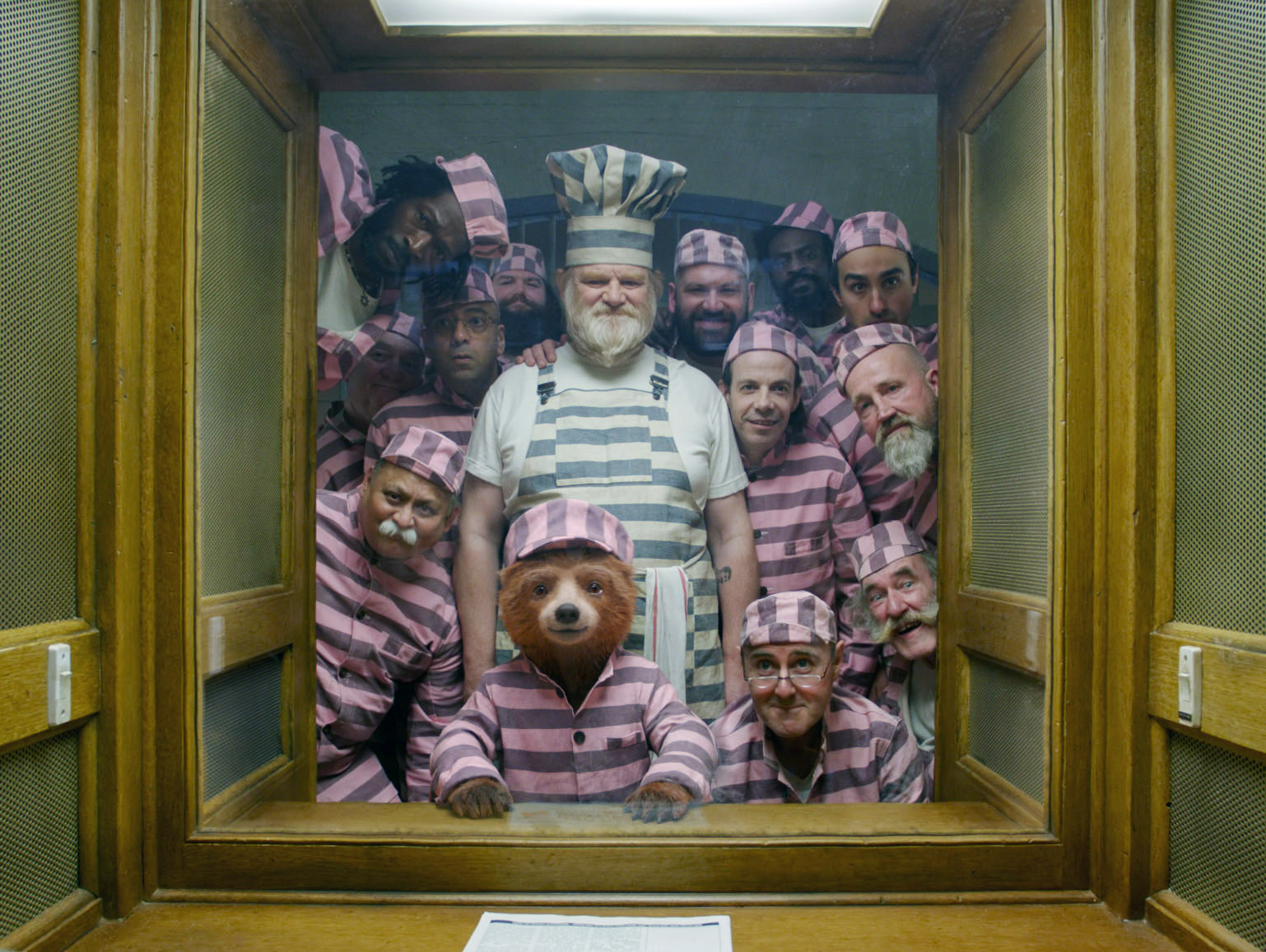 paddington the bear in a black and pink striped convict outfit surrounded by fellow inmates
