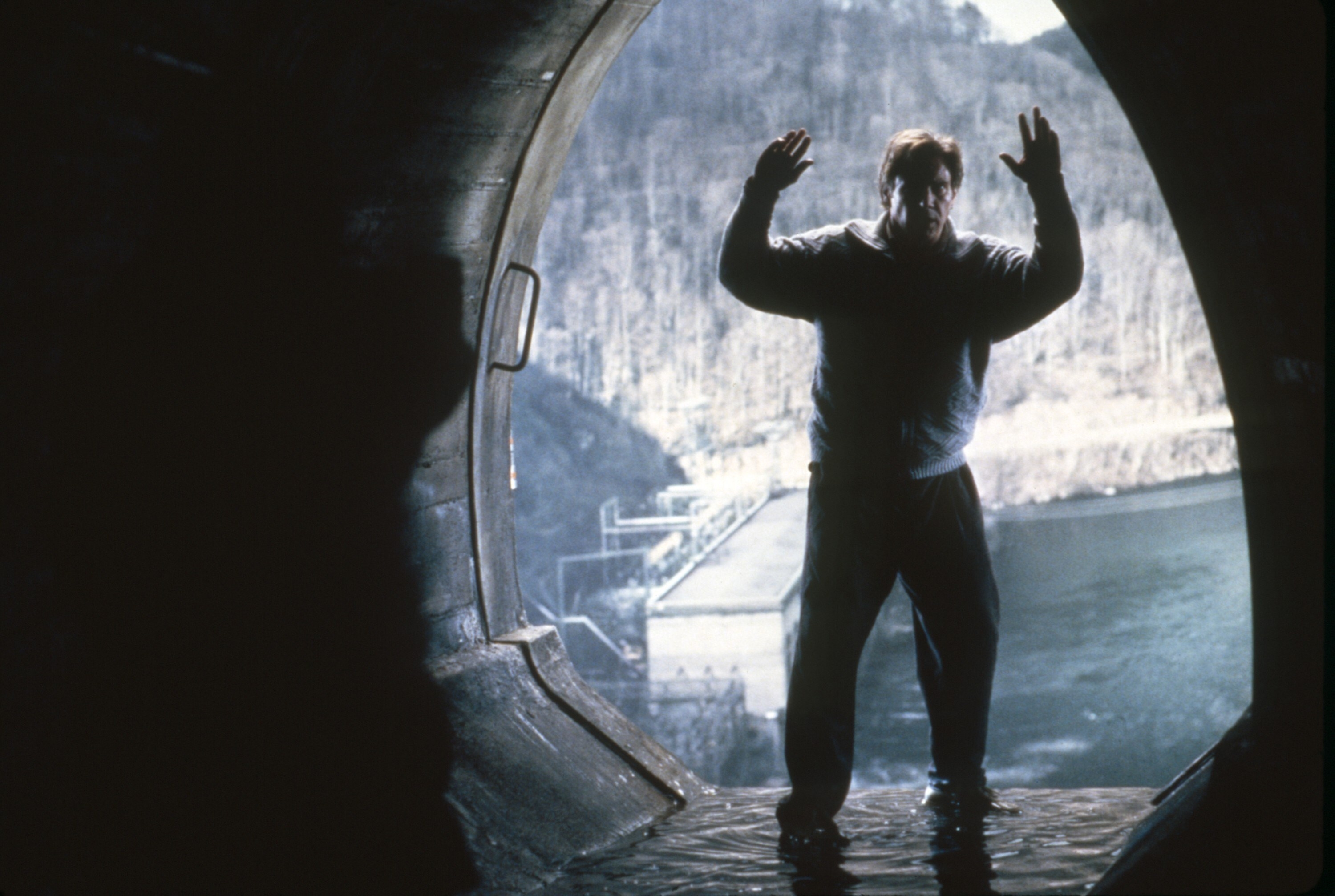 Harrison Ford with his hands up in surrender in a large drain pipe
