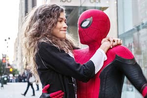 Peter Parker, in his Spider-Man suit, holds Michelle Jones on the street of New York City