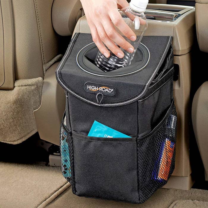 A person putting an empty bottle into the trash can in the car