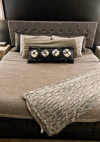 Reviewer image of made up bed with gray linen tufted headboard against black wall